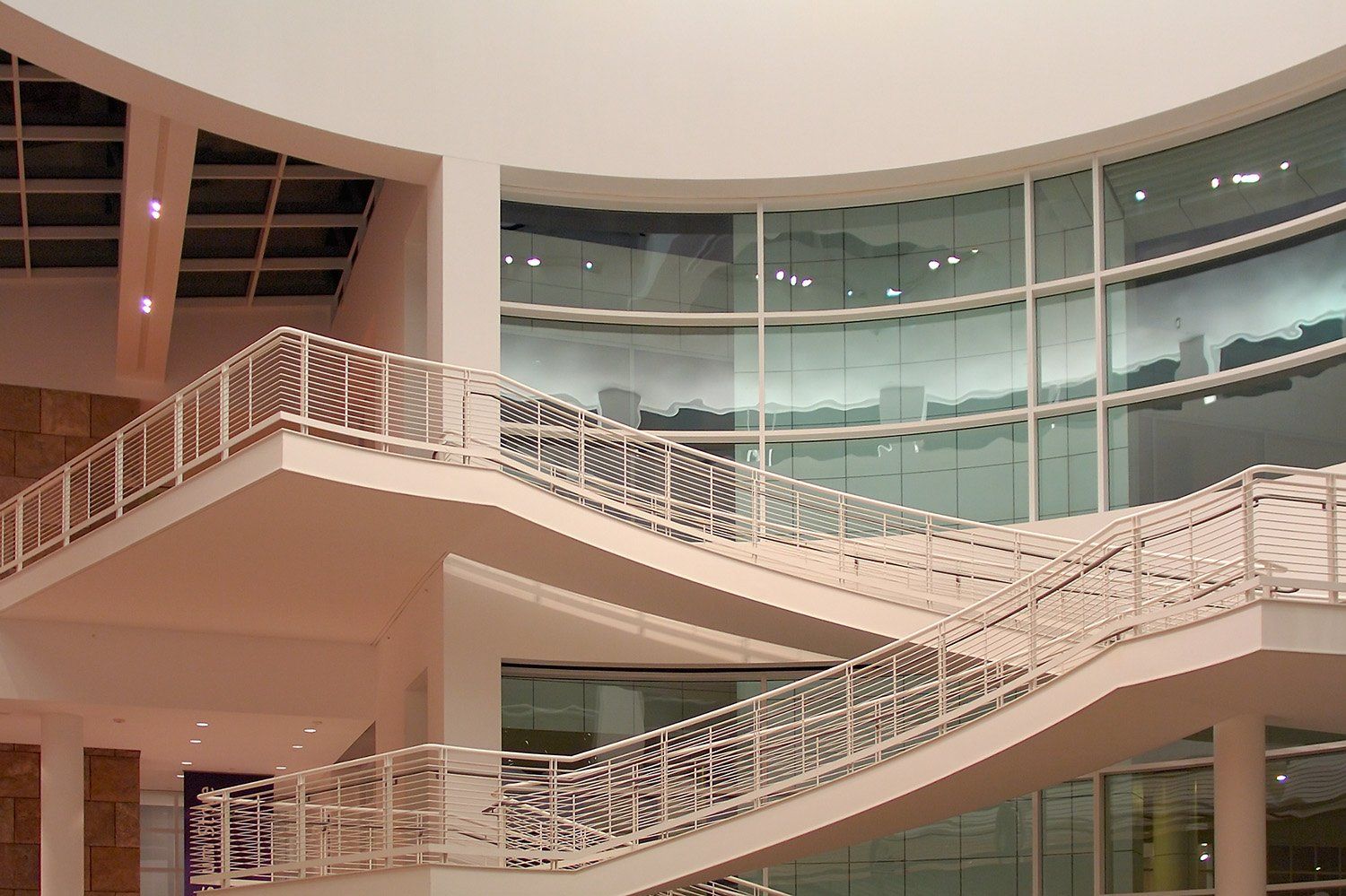 White staircases rising through a tall atrium of curved glass