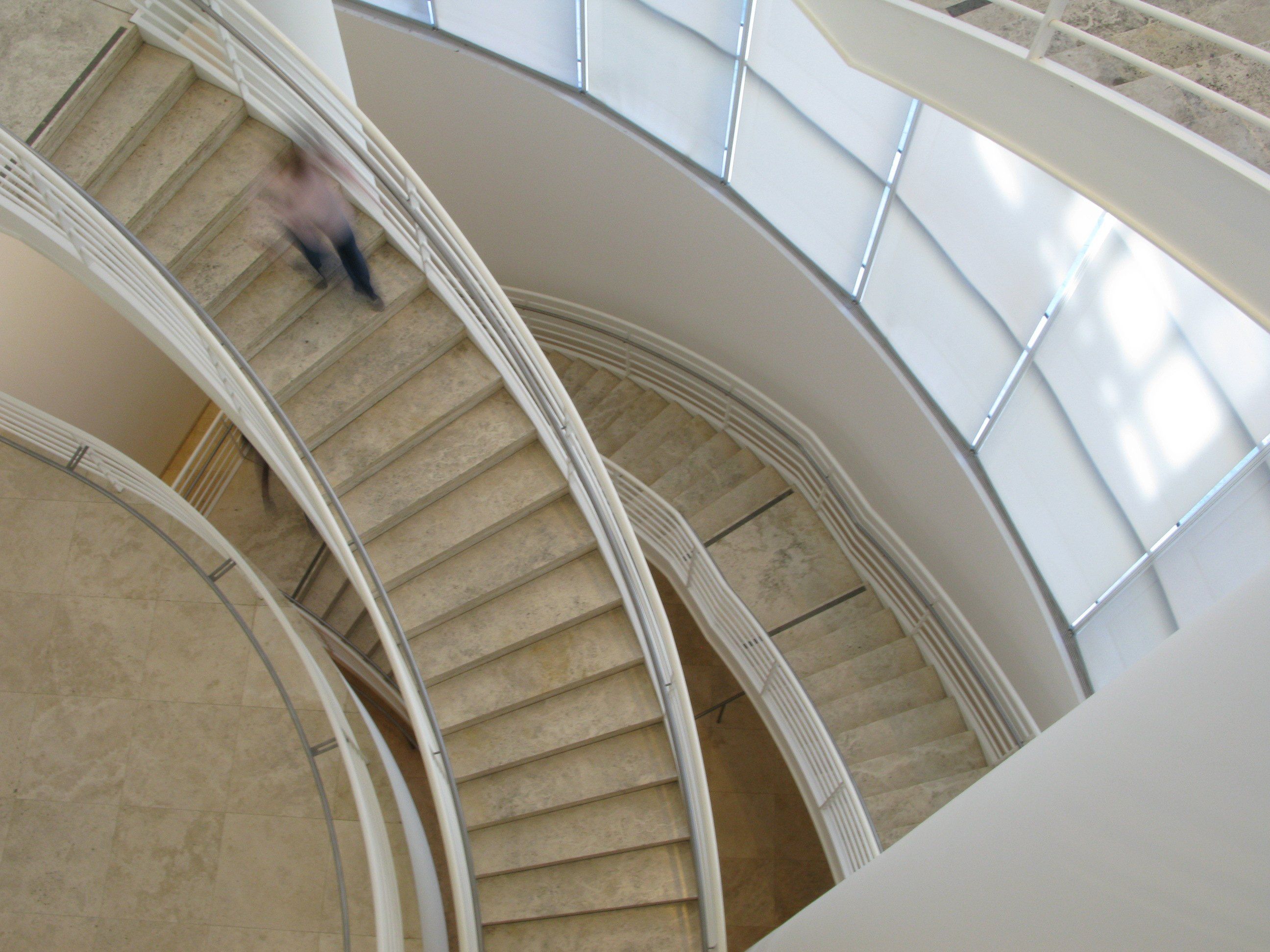 A spiral staircase seen from above, sweeping down through a skylit building